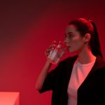 A fashionable woman drinks water in a red-lit room, creating a dramatic ambiance.