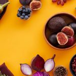 Colorful assortment of fruits, vegetables, and herbs on a vibrant yellow background in a flat lay style.